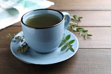 Cup of green tea and eucalyptus leaves on wooden table. Space for text