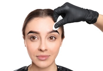 Beautician wiping tint from woman's eyebrows on white background, closeup
