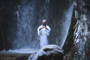 Man in traditional Japanese shugendo outfit doing waterfall meditation in winter with ice and snow