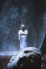 Fototapeta na wymiar Man in traditional Japanese shugendo outfit doing waterfall meditation in winter with ice and snow