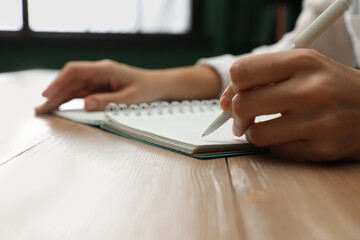 Left-handed woman writing in notebook at wooden table indoors, closeup