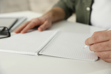 Fototapeta premium Left-handed man writing in notebook at white table, closeup