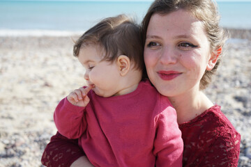 Happy family moment of a young mom enjoying a day on the beach with her baby