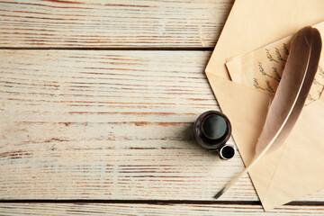 Feather pen, bottle of ink and letter on white wooden table, flat lay. Space for text