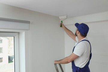 Handyman painting ceiling with white dye indoors, space for text