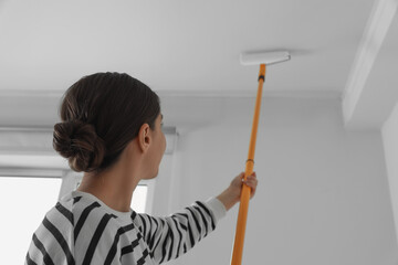 Young woman painting ceiling with white dye indoors, back view