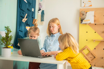 Children receive education at home in a classroom with a laptop, online courses for kids, three caucasian girls have fun and watch cartoons