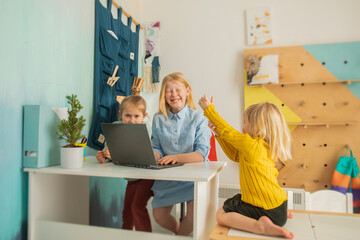 Children receive education at home in a classroom with a laptop, online courses for kids, three caucasian girls have fun and watch cartoons