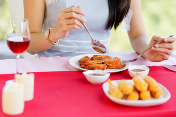 Woman eating chicken wings and glass of wine in food shop