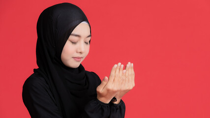 Asian Muslim women wear a black hijab, close their eyes, do religious activities, pray. Conceptual for religion On a red background