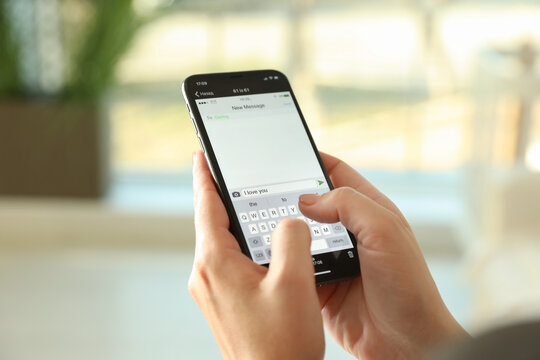 Woman writing message with text I Love You on smartphone against blurred background, closeup