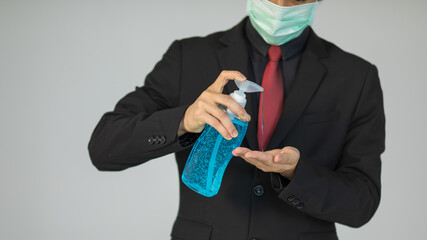Businessman in suit and wearing protective hygiene mask holding alcohol gel and pouring on hand for demonstrating how to wash and sterilize hands for coronavirus protection