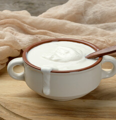 sour cream in a brown ceramic bowl with a wooden spoon on a wooden board