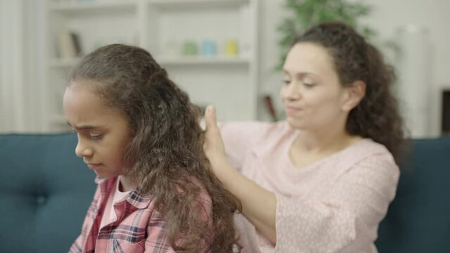 Mother trying to comb daughters tangled curly hair pain expression on girls face