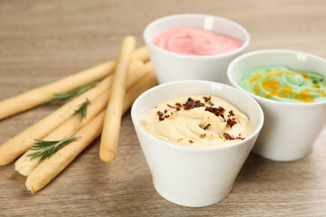 Different kinds of tasty hummus served with bread sticks on wooden table