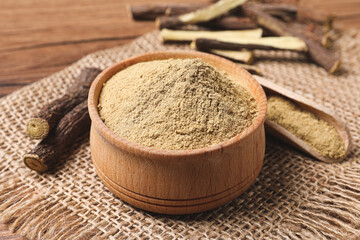 Dried sticks of liquorice root and powder on wooden table, closeup