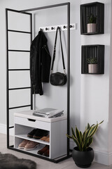 Stylish storage cabinet with different pairs of shoes near white wall in hall