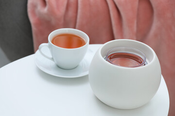 Wax air freshener and cup of hot tea on white table indoors. Interior element