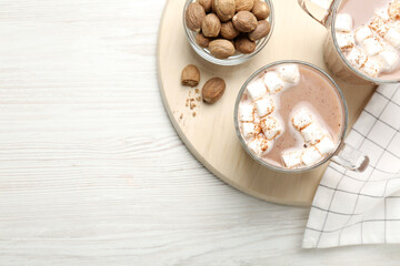Fototapeta na wymiar Cocoa drink with nutmegs and marshmallows on white wooden table, flat lay. Space for text