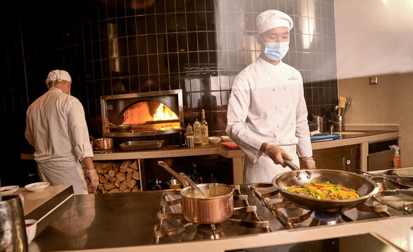 Asian Cook Keeping Peppers In Pan Over Stove Burner