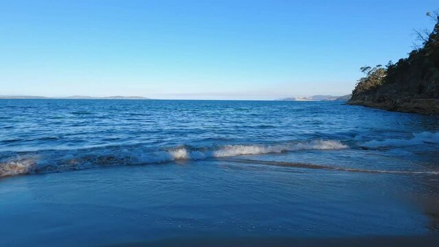 pristine beach in South Tasmania with blue waves of the ocean on the sand surrounded by rocky coastline