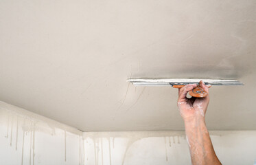 Hand of builder worker spacks ceiling with putty plaster aligning ceiling with spatula. Renovation and construction works