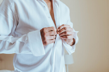 Novio poniéndose camisa. Preparativos el día de la boda para el novio. Manos de hombre abrochando...
