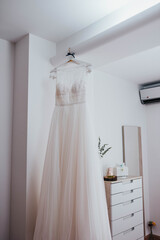 Fototapeta na wymiar Vestido de novia blanco en habitación. Vestido colgado. Preparativos el día de la boda en casa de la novia.