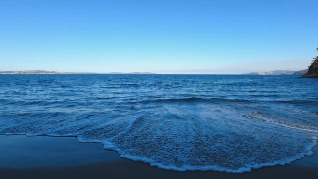 pristine beach in South Tasmania with blue waves of the ocean on the sand surrounded by rocky coastline