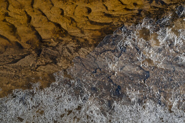 Spring beautiful patterns of ice crust and patterned brownish bottom in a small brook