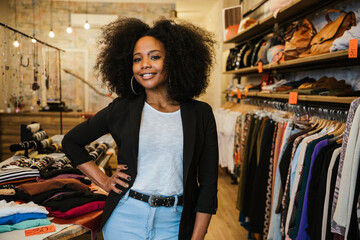 Professional portrait of a young beautiful owner of dress shop at entrance of commercial activity -...