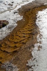 Curved streambed with a patterned bottom and icy banks during the spring thaw