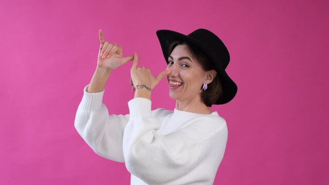 Woman in casual white sweater and hat on pink background isolated funny crazy does grimaces fool day     