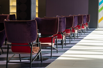 A row of tables with soft comfortable violet chairs for visitors to the food court of a modern shopping center.