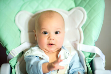 A funny little boy is sitting in a feeding chair.Family morning at home. . image with selective focus
