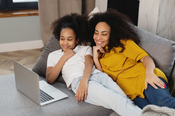 African american mother and her daughter using laptop lying on couch.
