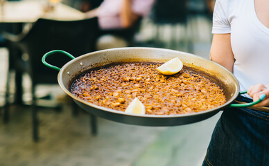 waiter holding paella with seafood and squid close-up - Spanish food