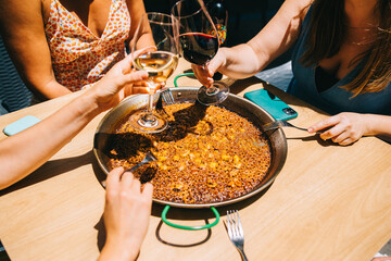 Time to eat paella. Several hands with wine drinks begin to eat paella with seafood and squid at a table in a restaurant
