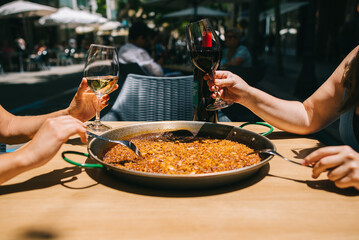 Time to eat paella. Several hands with wine drinks begin to eat paella with seafood and squid at a table in a restaurant