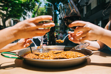 two girls holding drinks wine start eating paella with seafood and squid at a table in a restaurant