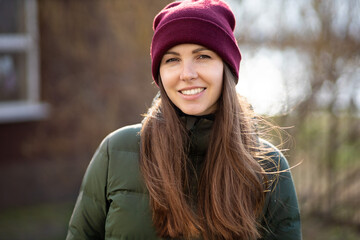 portrait of a cute young brunette girl with a beautiful smile in a warm hat and jacket in the afternoon in the background light