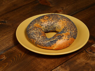 Fresh bagel with poppy seeds on a yellow plate on a wooden table