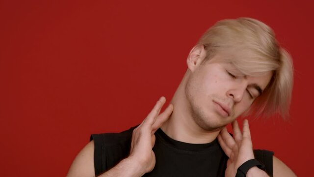 Fitness training. Young sporty caucasian guy warming up his neck before sport workout, red background