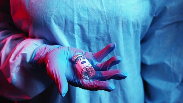 Covid-19 vaccine. Disease prevention. Global health immunization. Inoculation dose vial in doctor hand in blue ppe protective glove in red neon light.