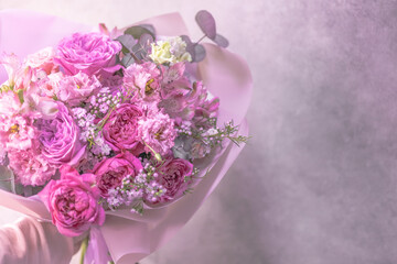 A lush bouquet of light pink, purple, white cute delicate small roses of different sizes, flowers of green leaves. Paper packaging. Place for text