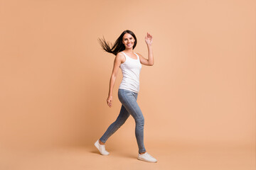 Fototapeta na wymiar Full size profile photo of optimistic brunette girl go wave hand wear white top jeans sneakers isolated on beige background
