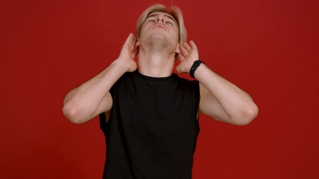 Right training. Young sporty man warming up his neck, swinging it to both sides, red background, slow motion