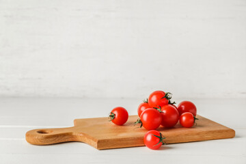Cutting board with tomatoes on light wooden background