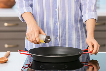 Woman pouring oil onto frying pan in kitchen