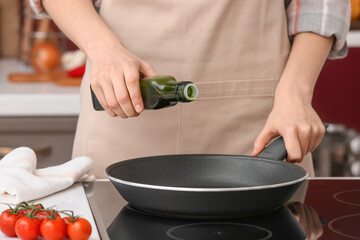 Woman pouring olive oil onto frying pan in kitchen